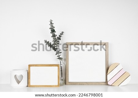 Mock up wood frames with rustic Valentines Day wooden heart decor, eucalyptus branch and candle holder. White shelf against a white wall. Copy space.