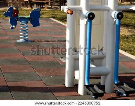 Fitness machine and background swinging kid horse in public park.