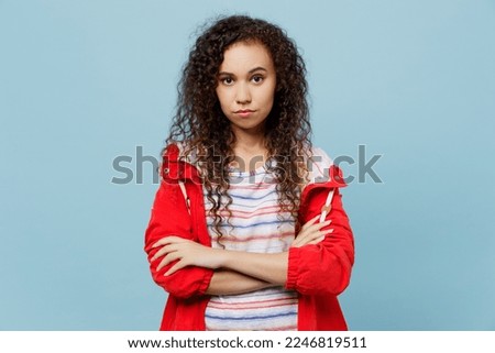Young indignant sad woman of African American ethnicity 20s wear red jacket look camera hold hands crossed folded isolated on plain pastel light blue cyan background. Wet fall weather season concept