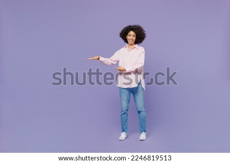 Full body smile young woman of African American ethnicity 20s wear pink striped shirt show height scale with arms hands look camera isolated on plain pastel light purple background studio portrait.