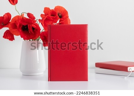 Office desk, red book cover mockup, vase with red flowers poppies. Front view. Place for text, copy space, mockup