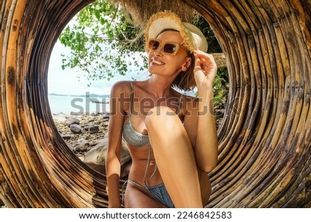 Happy Woman, solo traveler relaxing on a swing, on the paradise beach. Female tourist in bikini and summer hat . Wanderlust and vacation concept.
