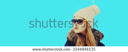Winter portrait of beautiful young blonde woman wearing hat on blue background