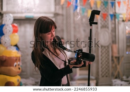 Girl photographer with a camera at work on the set in the banquet hall. A young beautiful woman - a professional photographer with a camera and a flash takes pictures on a holiday in a decorated hall