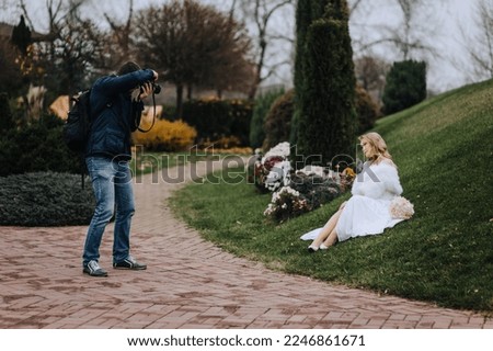 A professional wedding photographer works with a model bride in a white dress in a park outdoors, taking pictures, making portraits. Photography, concept, art.