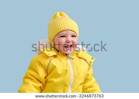 Happy toddler baby in winter clothes snowsuit on studio blue background. A child in a warm yellow jumpsuit with a hood. Kid aged one year five months Royalty-Free Stock Photo #2246873763