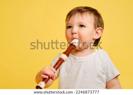 Toddler baby plays the flute, a child with a wind musical instrument on a studio yellow background. Happy child musician playing block flute. Kid is a boy aged one year four months Royalty-Free Stock Photo #2246873777