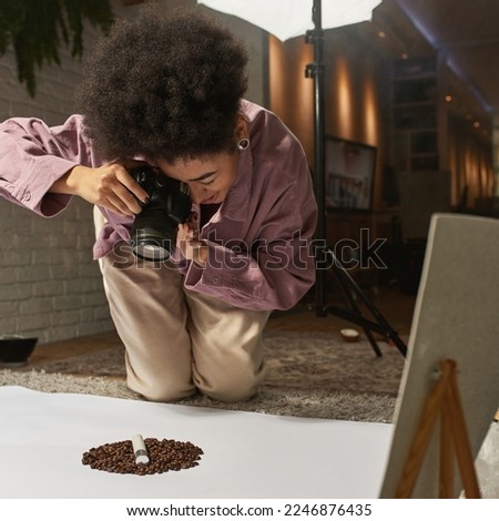 Black female photographer taking photo of coffee beans and cosmetic product on digital camera at home studio. Beauty and body care content for photostocks, commerce, social networks and advertising