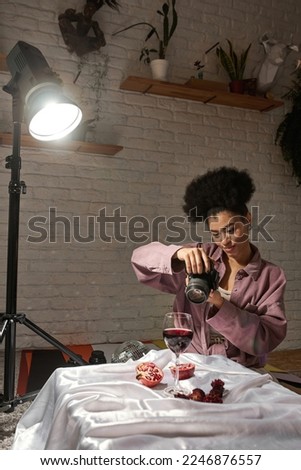 Girl photographer take photo of sliced grapefruit, dry rose flowers, glass with wine and necklace on digital camera at home studio. Content for photostocks, commerce, social networks and advertising