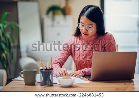 Vietnamese woman using laptop while working at home and sitting at the table and writing notes. Asian businesswoman or student working on a research project. Copy space.