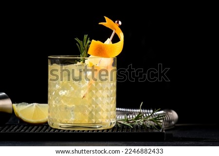 Penicillin alcoholic cocktail with scotch, whiskey, honey ginger syrup, lemon juice and ice in glass garnished with orange zest. Black background Royalty-Free Stock Photo #2246882433