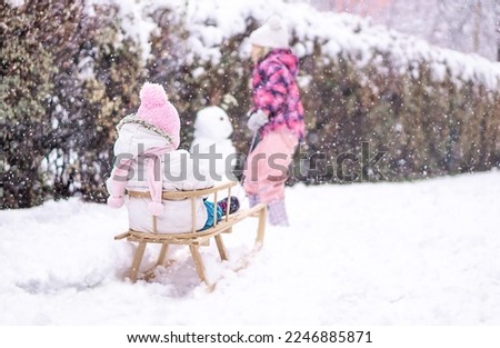 Girl sledding her sister in snow park. Family vacation in winter.