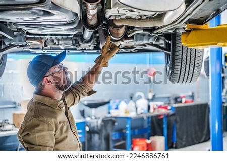 Professional Caucasian Mechanic Standing Under the Vehicle Lifted on Car Lift Checking the Condition of Catalytic Converter. Automotive Theme. Royalty-Free Stock Photo #2246886761