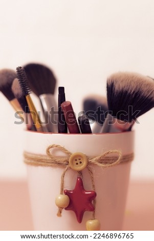A set of makeup brushes and makeup pencils in a white pot tied with jute thread with a star on a pink and white background, close-up side view with depth of field. 