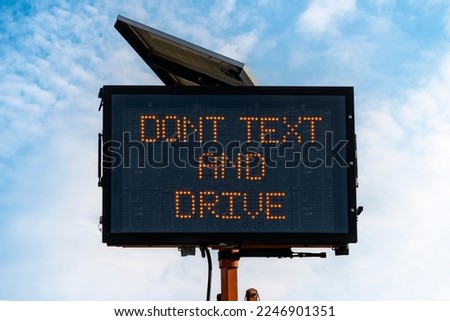 Photo illustration of digital road sign in front of blue sky with text Dont text and drive to convey a concept of distracted driving prevention and awareness. 