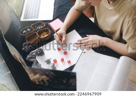 Role playing tabletop and board games hobby concept. Woman hand writing for create story setup adventure sword and magic theme. Foreground with blur monsters miniatures and dice. Royalty-Free Stock Photo #2246967909