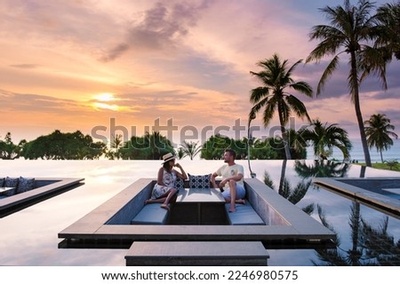 couple watching the sunset in an infinity pool on a luxury vacation in Thailand, man and woman watching the sunset on the edge of a pool in Thailand on vacation Royalty-Free Stock Photo #2246980575