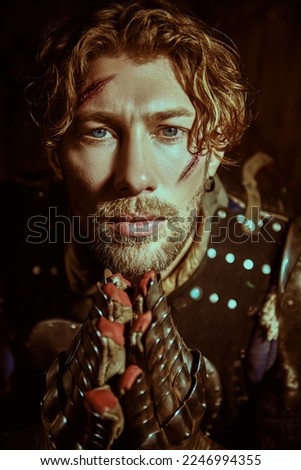 Portrait of a handsome medieval knight with scars on his face in armor praying before the fight. Studio portrait on a black background.