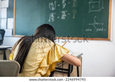 Education. Back view of school girl on lesson in classroom write hardworking on blackboard, primary child is sitting lessons at table in school writing or drawing in notebook, Back to school concept Royalty-Free Stock Photo #2246994745