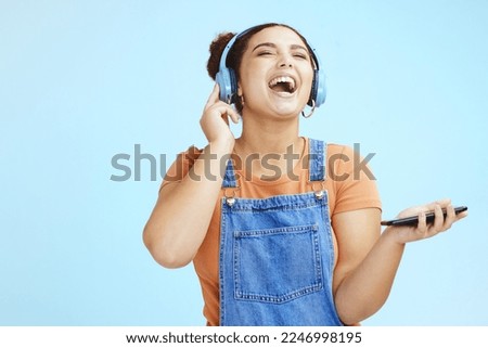 Mockup, headphones and woman with smartphone, happy or connection on blue studio background. Fun, female or girl laughing, cellphone for music or headset for podcast, online streaming or social media