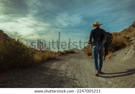 Rear view of adult man in cowboy hat walking on dirt road
