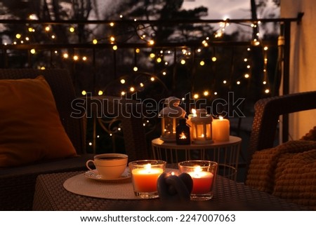 Beautiful view of garden furniture with pillow, soft blanket and burning candles at balcony Royalty-Free Stock Photo #2247007063