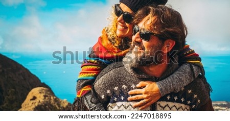 Excited and overjoyed happy mature young couple man and woman having fun together. Man carrying woman and both smile and laugh a lot in outdoor leisure activity. Concept of travel and happiness Royalty-Free Stock Photo #2247018895