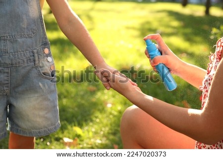 Mother applying insect repellent onto girl's hand in park, closeup Royalty-Free Stock Photo #2247020373