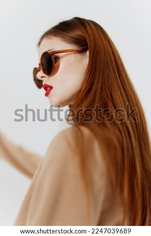 A stylish young woman in glasses and a beige coat poses on a white background in designer clothes at a catalog photo shoot in the studio
