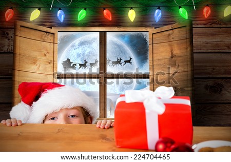 Festive boy peeking over table against santa delivery presents to village