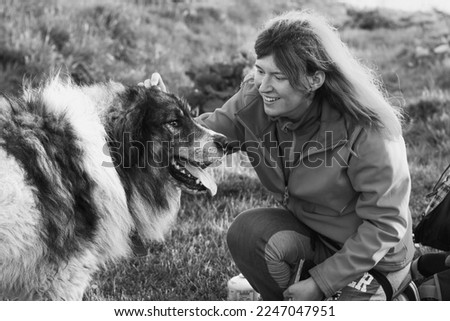 Happy lady strokes carpathian shepherd dog monochrome scenic photography. Picture of person with meadow on background. High quality wallpaper. Photo concept for ads, travel blog, magazine, article