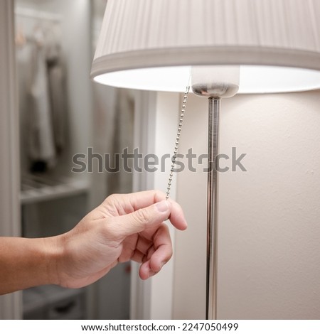 Male hand turn off the light on torchiere lamp in bedroom. Saving electricity energy at night. Switch off lighting equipment for bedtime. Royalty-Free Stock Photo #2247050499