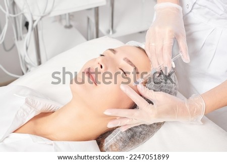 Cosmetologist makes rejuvenation injection in woman face skin, anti aging revitalization cosmetic procedure in beauty spa salon. Beautician hands in gloves makes facial acid injection treatment Royalty-Free Stock Photo #2247051899