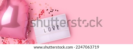 Word Love. Banner with lightbox, confetti and inflatable foil balloon in a heart shape on a pink pastel background. Selective focus.