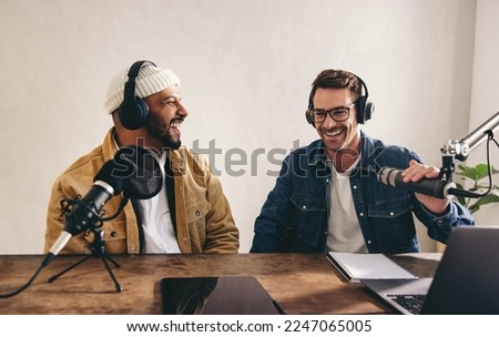 College radio dj's laughing and having a good time on air. Two happy young men recording a live audio broadcast in a studio. Cheerful content creators co-hosting an internet podcast.