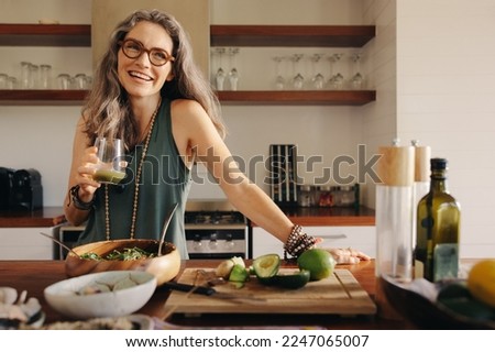 Healthy senior woman smiling while holding some green juice in her kitchen. Mature woman serving herself wholesome vegan food at home. Woman taking care of her aging body with a plant-based diet. Royalty-Free Stock Photo #2247065007