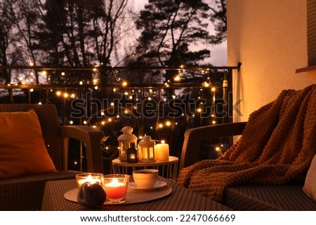 Beautiful view of garden furniture with pillow, soft blanket and burning candles at balcony Royalty-Free Stock Photo #2247066669