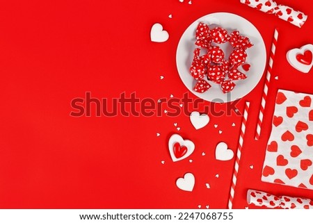 Valentine's Day decoration with candy, heart ornaments and sugar sprinkles on red background with copy space