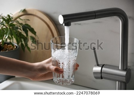 Woman filling glass with tap water from faucet in kitchen, closeup Royalty-Free Stock Photo #2247078069