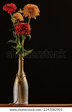 Homemade silver and gold plated wine bottle vase with a bouquet of zinnia flowers on a dark background