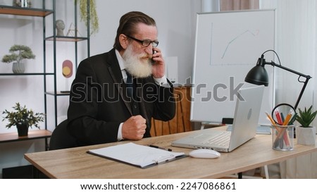 Conflict, quarrel, negotiation. Angry senior businessman ceo making webcam laptop mobile phone online call at home office desk. Upset mad freelancer grandfather old man talking conversation indoors Royalty-Free Stock Photo #2247086861