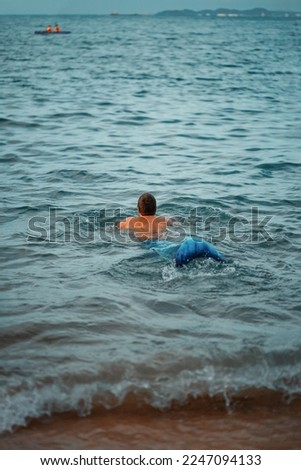 Mermen swims in the sea towards the people in the boat. Mermaid male swims towards people.