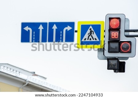 Road signs indicating the direction of movement, traffic lights with arrows, a pedestrian crossing sign on the street against the sky. Red traffic light.