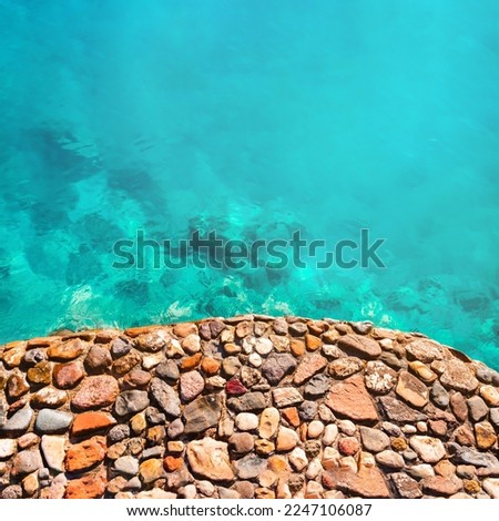 The transparent blue sea approaches the multi colored stone shore. The sea bay.