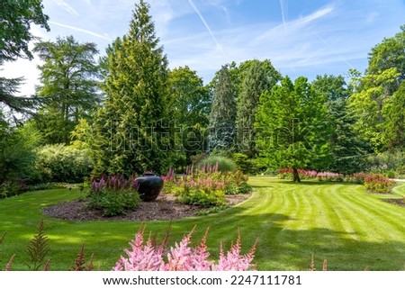 In this carefully mowed lawn is a large vase, surrounded by Astilbe and various types of trees and shrubs in an arboretum in Rotterdam, Netherlands Royalty-Free Stock Photo #2247111781