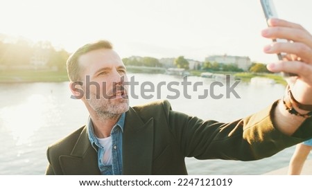 Close up, man makes selfie on mobile phone on the embankment of the river. Backlight