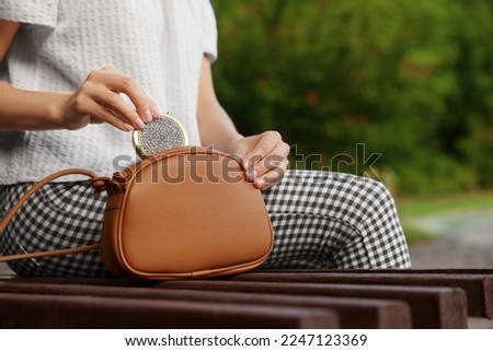 Woman taking cosmetic pocket mirror from bag on bench outdoors, closeup Royalty-Free Stock Photo #2247123369