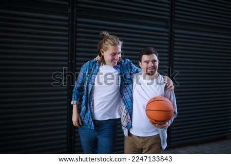 Man with down syndrome playing basketball outdoor with his friend. Concept of friendship and integration people with disability into society. Royalty-Free Stock Photo #2247133843