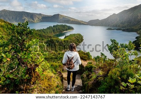 Woman tourist on hiking trail admiring scenic view of Lagoa do Fogo (Lake of Fire) - a crater lake on Sao Miguel Island, Azores, Portugal. Mountain hiking and wanderlust concept Royalty-Free Stock Photo #2247143767