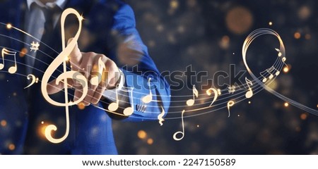 Musician pointing at staff with music notes and symbols on color background, closeup. Banner design Royalty-Free Stock Photo #2247150589